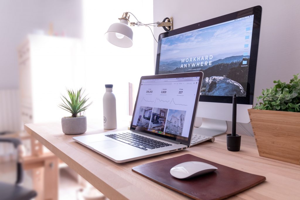 Picture Shows A Desk With A Plant On And Two Laptops. One Of The Screens Says 'Work Hard Anywhere'.